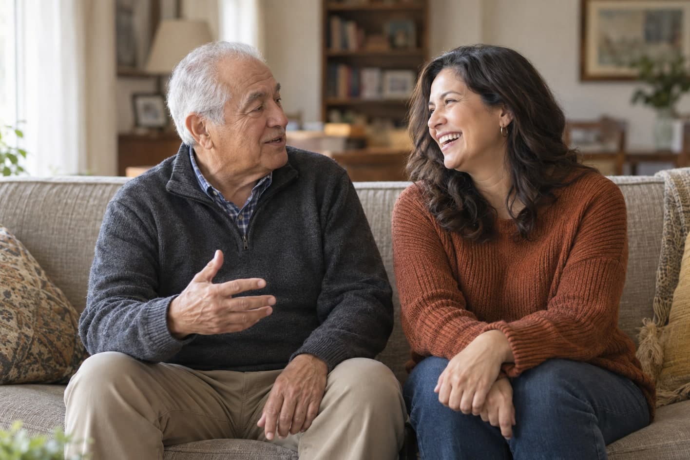 An older man and a younger woman talking and laughing on a living room sofa.